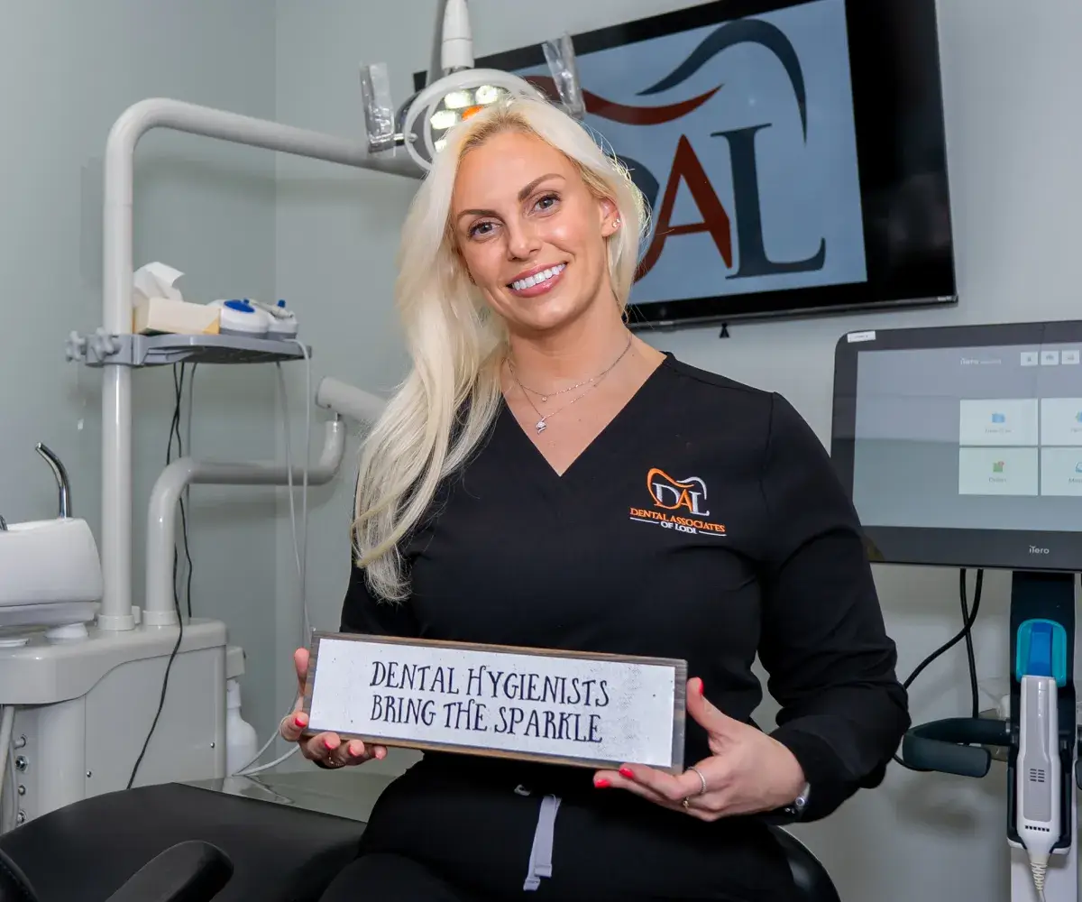 A dental hygienist smiles while holding a sign that reads, "Dental hygienists bring the sparkle."
