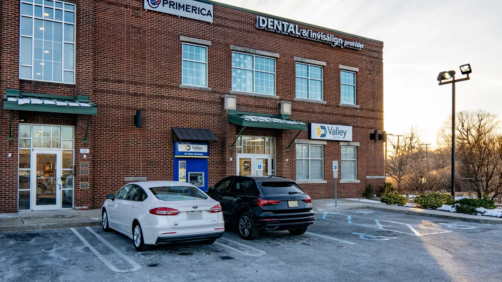 Two cars parked outside a brick building with signs for a dental office and bank.
