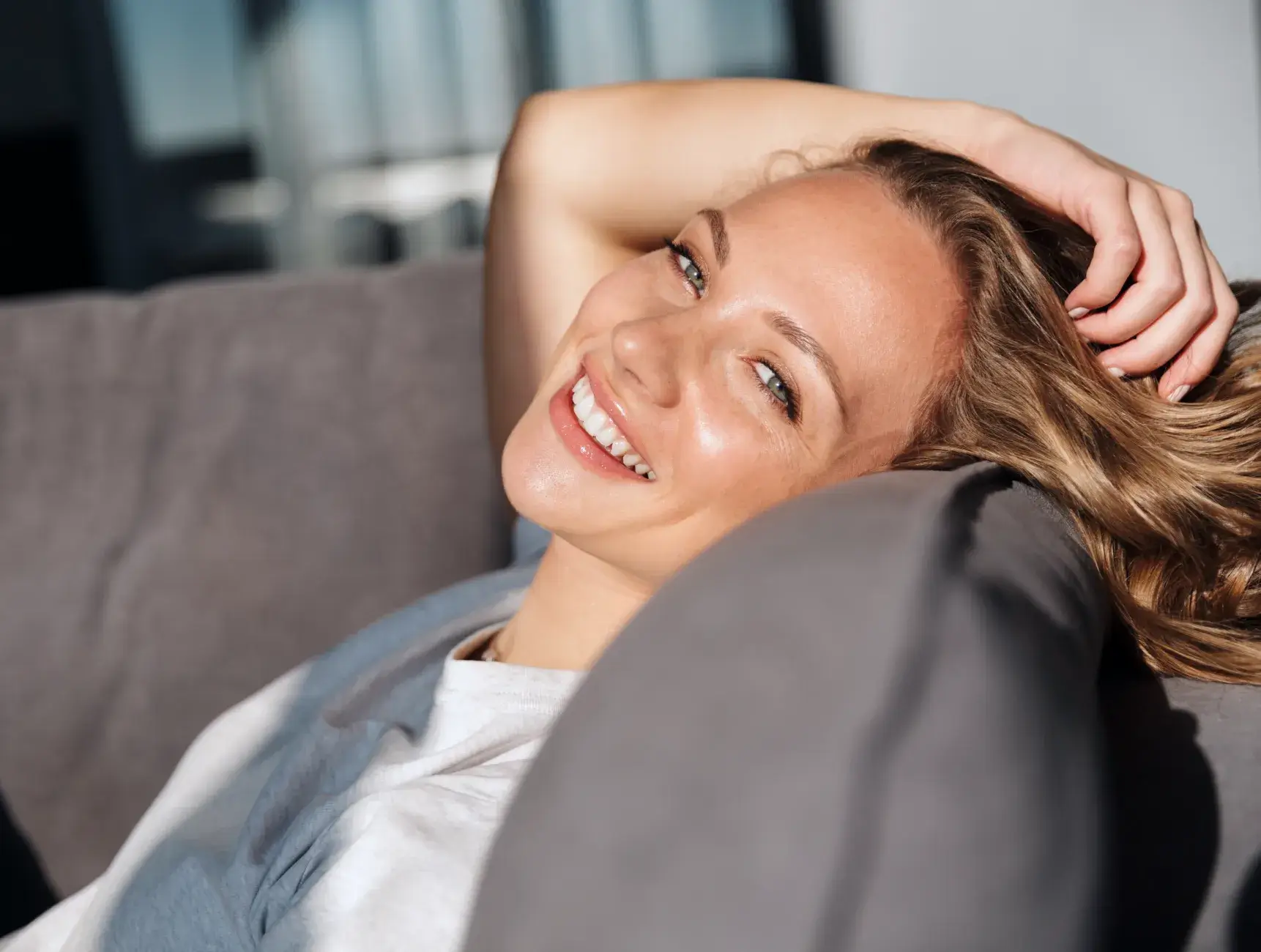 A beautiful woman laying on top of a gray couch.