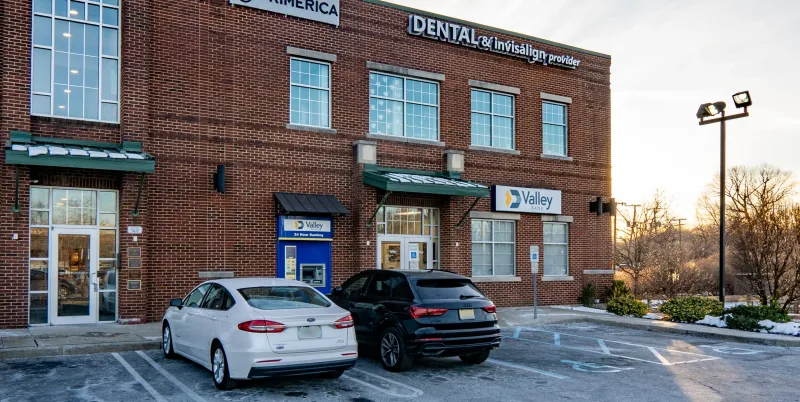 Two cars parked in front of a brick building housing Valley Bank and a dental office.