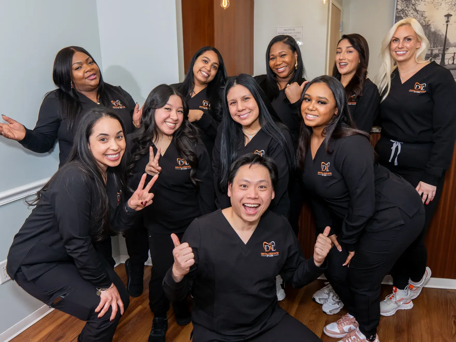A group of smiling people in matching dark outfits pose together in a hallway.