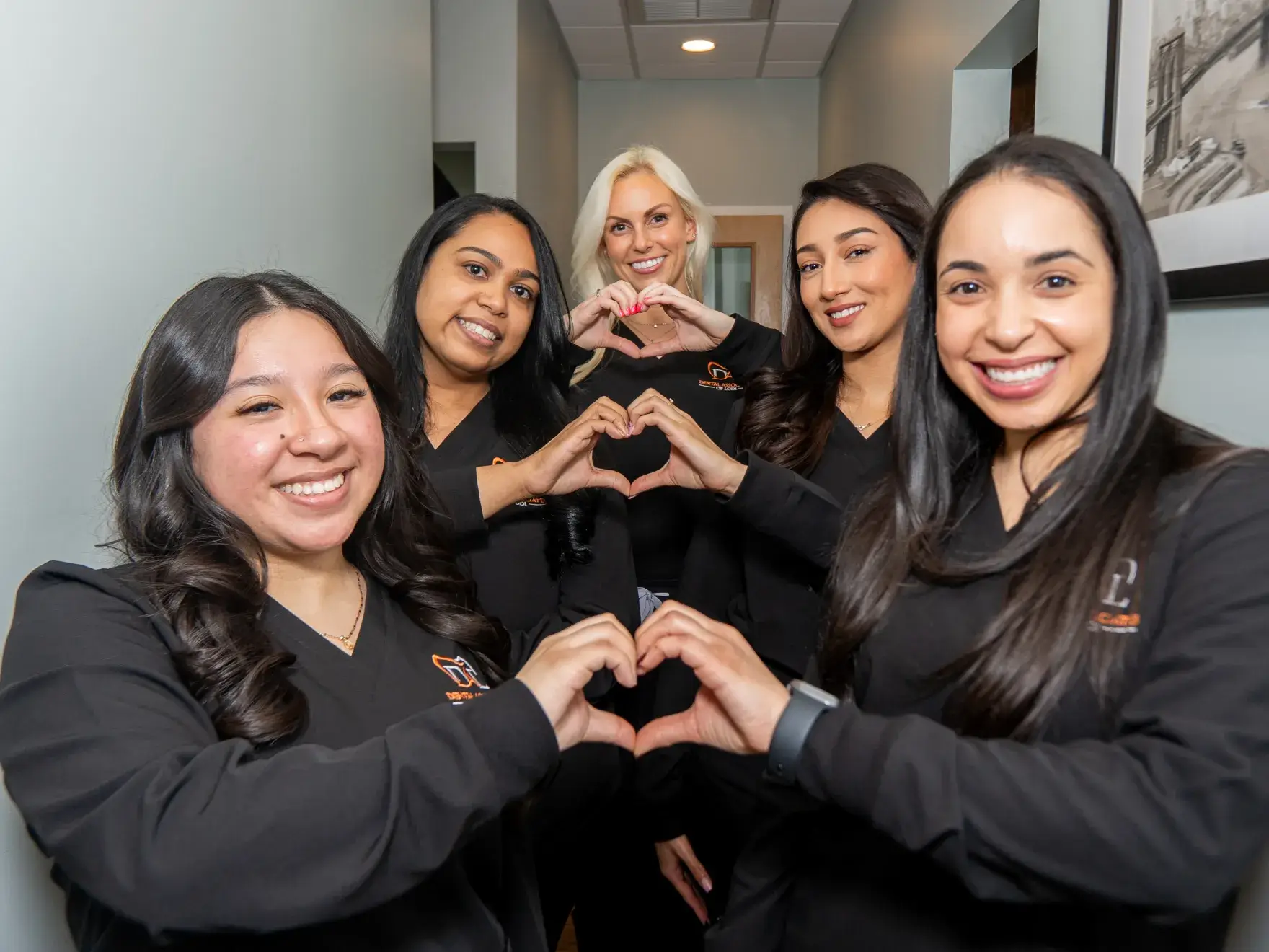 Five women in black uniforms making heart shapes with their hands.