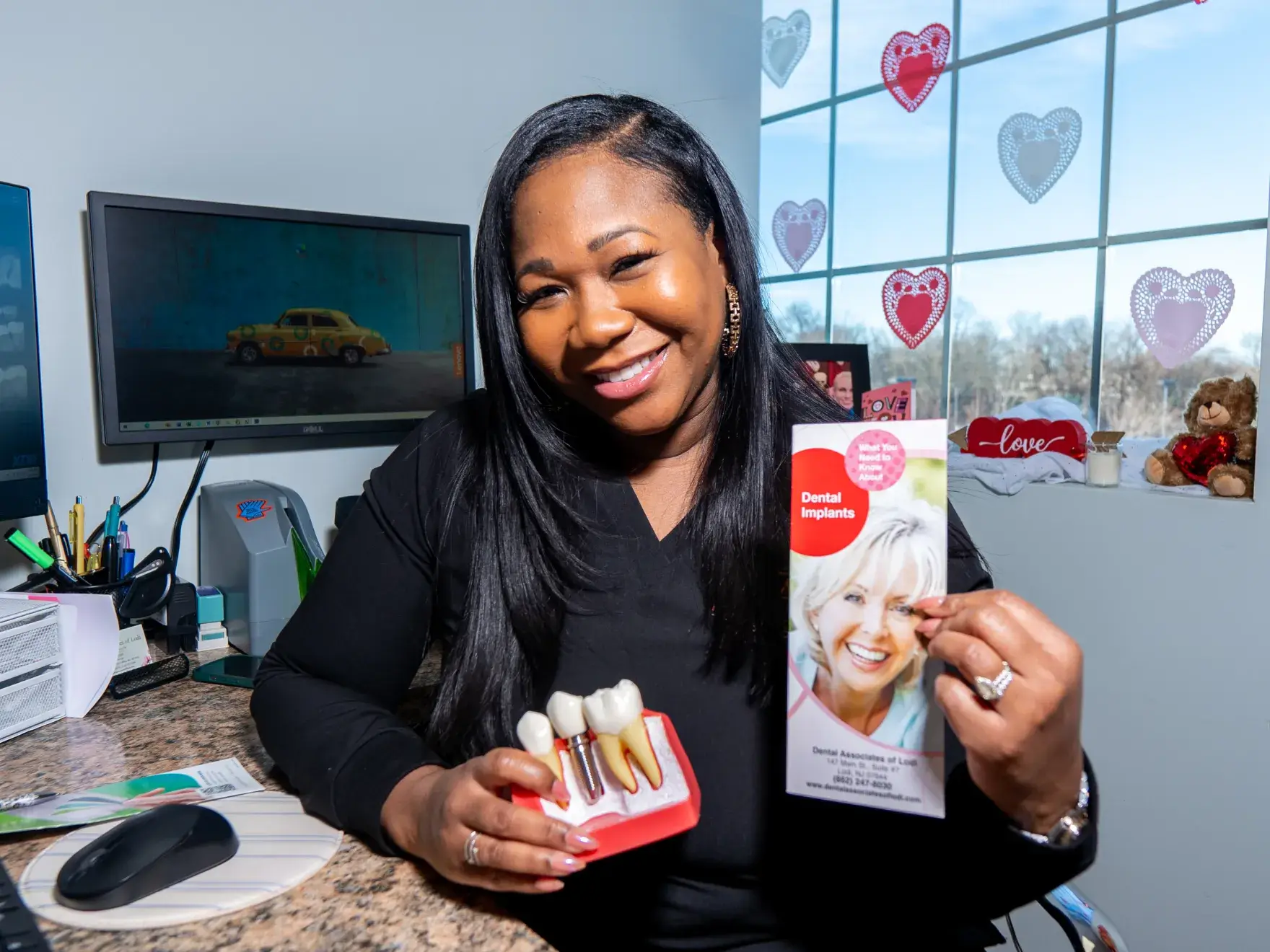 A smiling woman holds a dental implant model and a brochure.