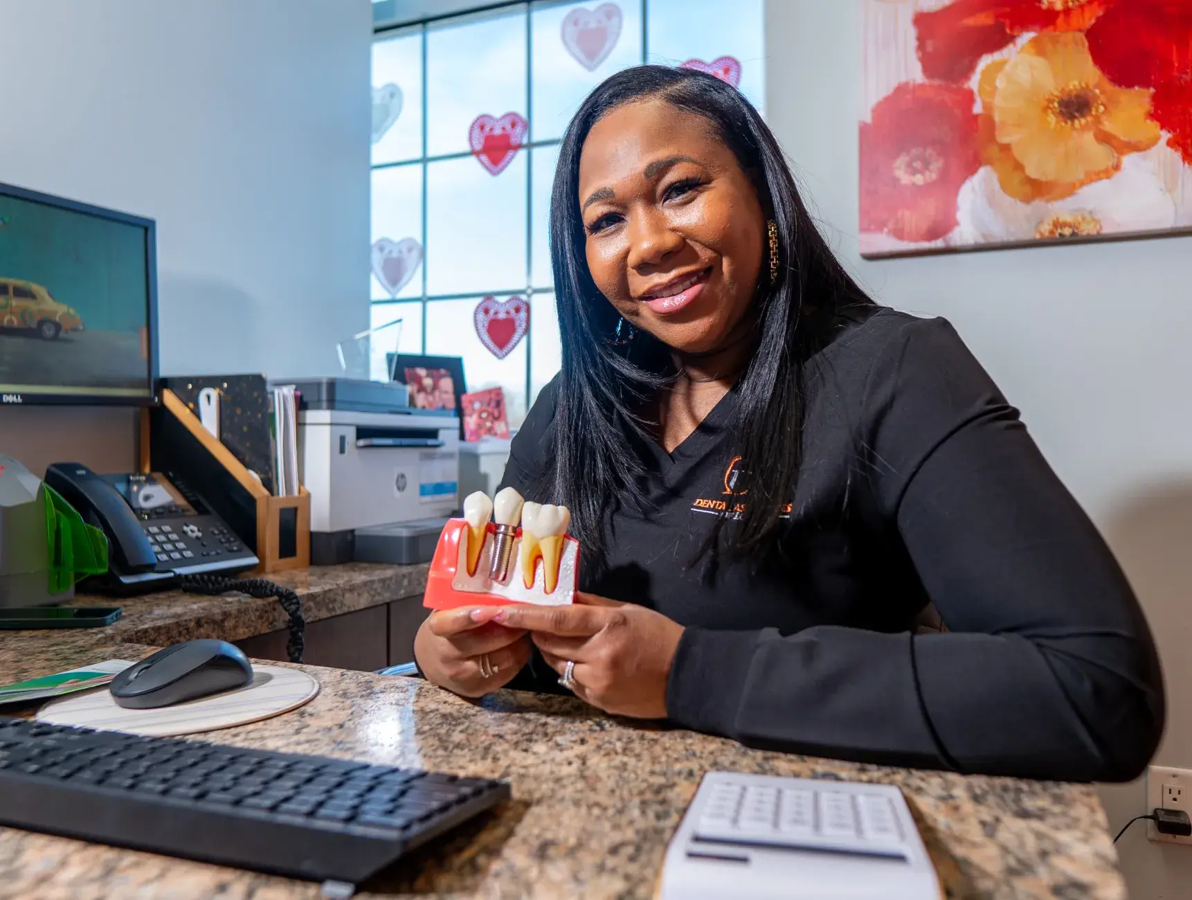 A woman in an office smiles while holding a dental model.