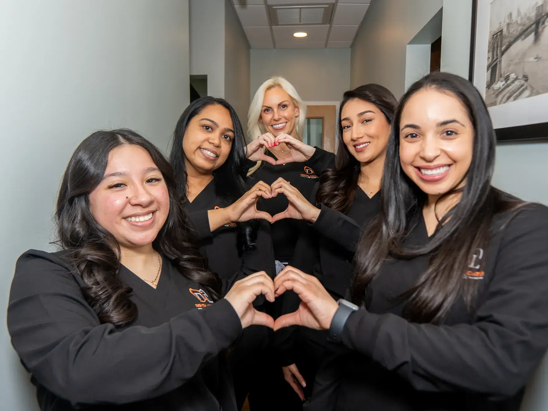 Five people in dark uniforms smiling and making heart shapes with their hands.