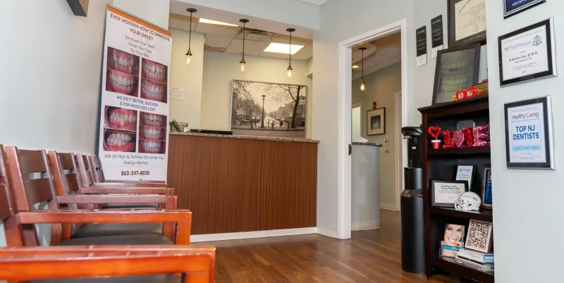 Dental office waiting area with wooden chairs, reception desk and TV.