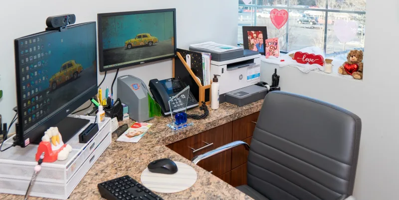 An office desk with dual monitors, a printer, keyboard, and paperwork.