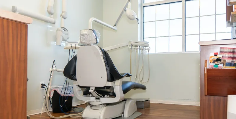 An empty dentist chair in a clean clinic room, facing a window.