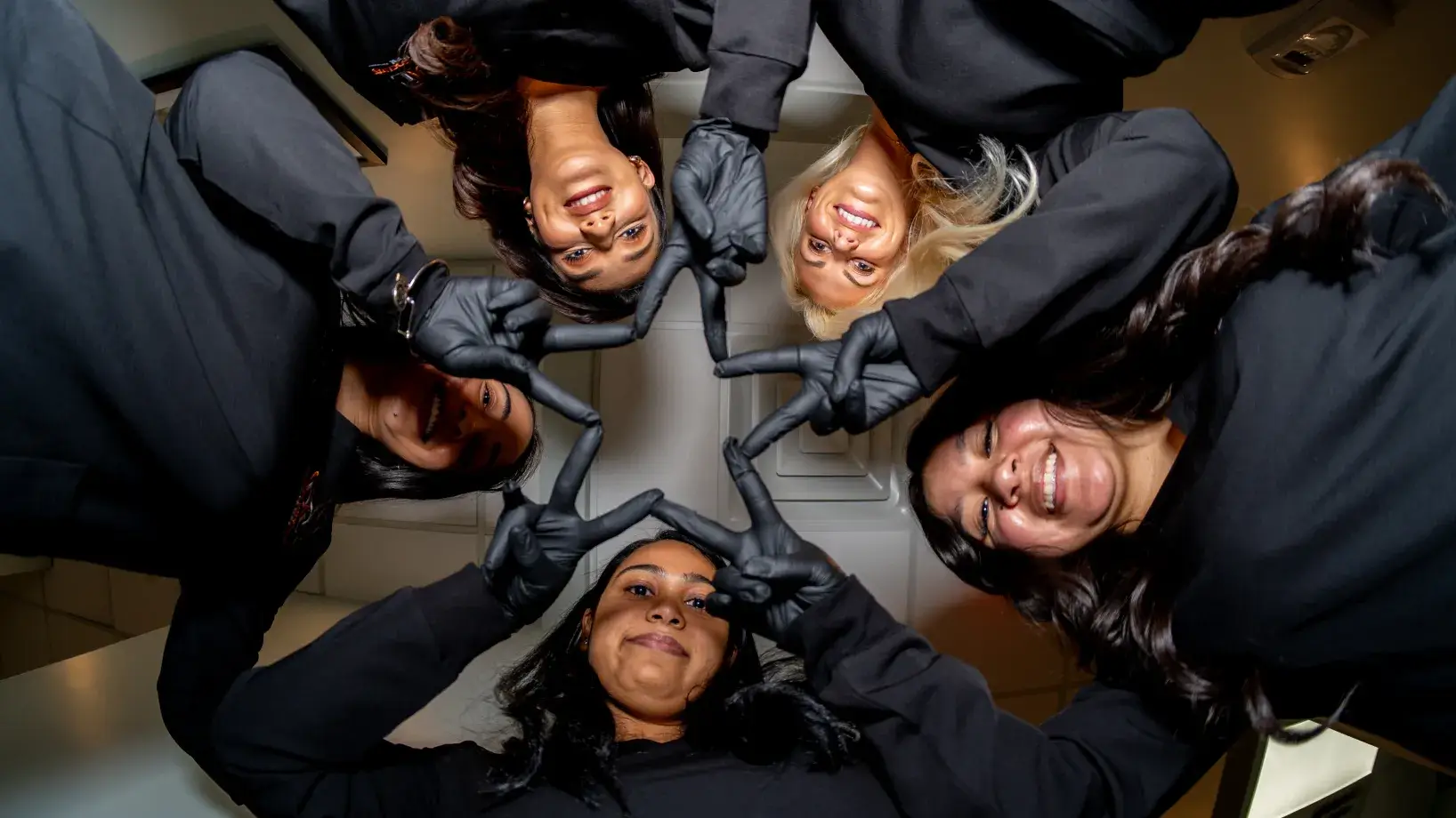 Five people wearing black shirts and gloves form a star shape with their hands, looking upwards.
