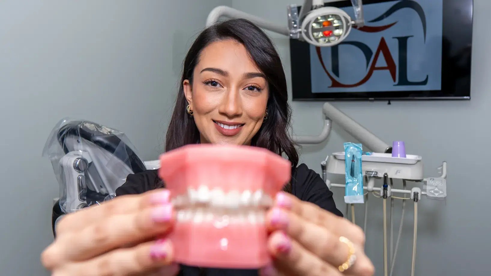 A woman smiling and holding a dental model in a dentist's office.