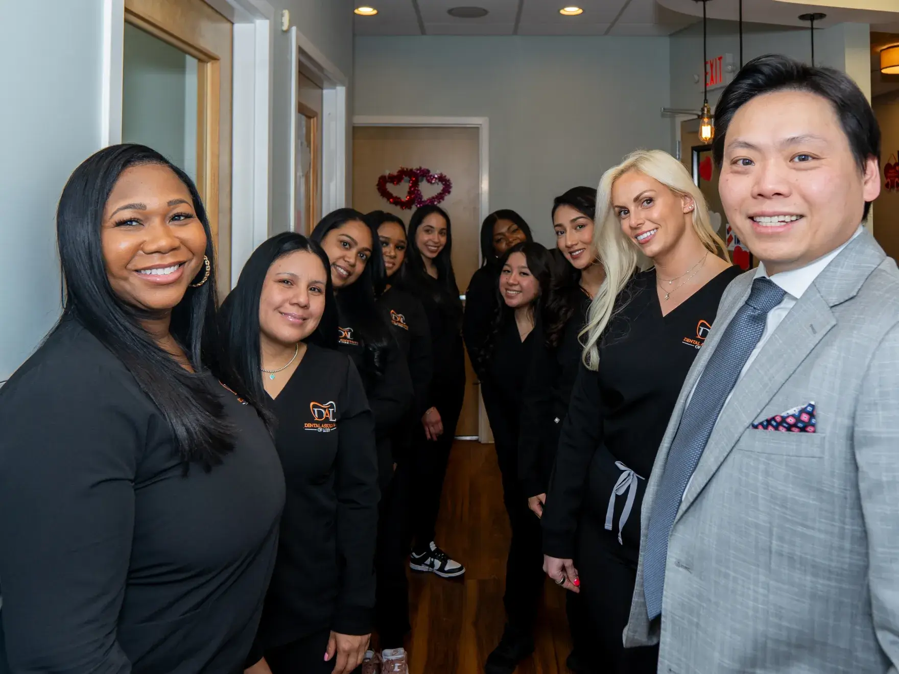 A group of people, mostly in black attire, smiling in a hallway.